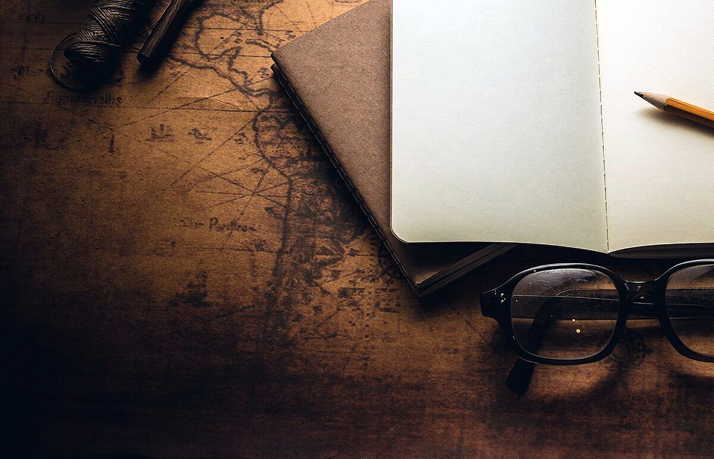 Carnet ouvert, crayon, lunettes et loupe posés sur une ancienne carte du monde