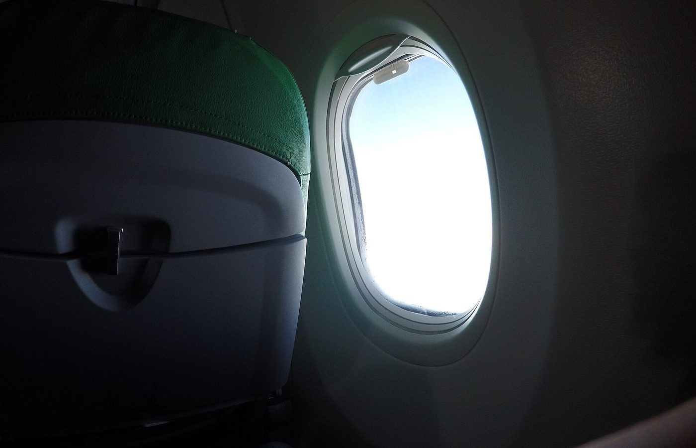 Hublot d’avion ouvert sur un ciel lumineux, vu depuis la cabine